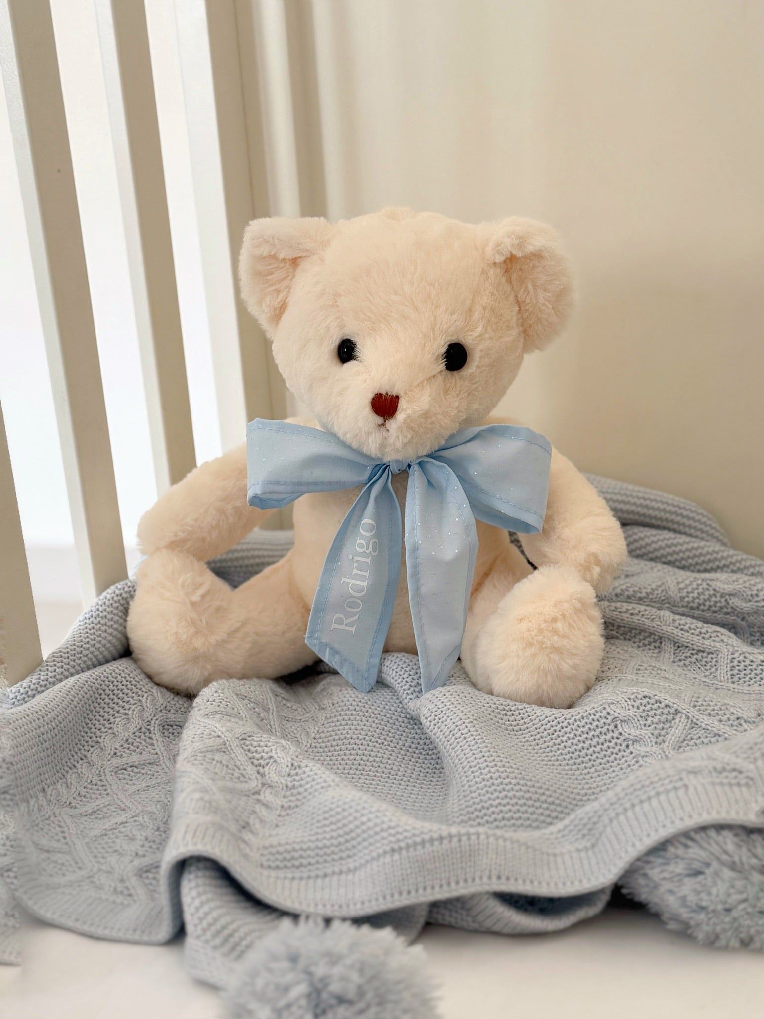 Oso de peluche con listón celeste decorando nursery, regalo personalizado para bebé