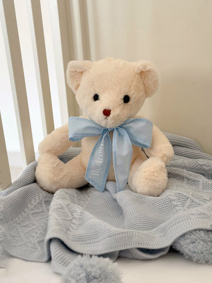 Oso de peluche con listón celeste decorando nursery, regalo personalizado para bebé